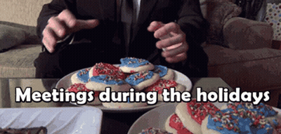 A Man In A Suit Is Sitting At A Table With A Plate Of Cookies And The Words Meetings During The Holidays Above Him GIF