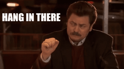 A Man In A Suit Is Sitting At A Table With His Fist In The Air And The Words `` Hang In There '' Behind Him . GIF
