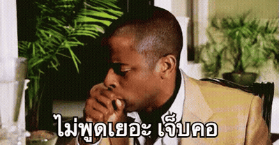A Man In A Suit Is Sitting At A Table With His Hand In His Mouth And A Plant In The Background . GIF
