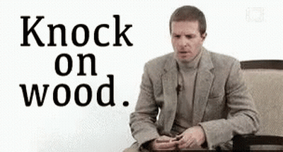 A Man In A Suit Is Sitting At A Table With The Words `` Knock On Wood '' . GIF
