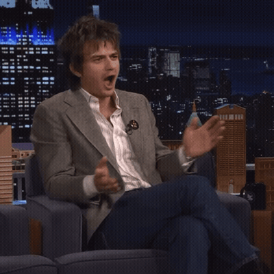 A Man In A Suit Is Sitting In A Chair And Making A Funny Face GIF