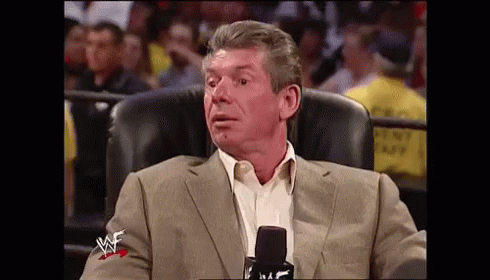 A Man In A Suit Is Sitting In A Chair In Front Of A Microphone With A W Logo On His Jacket . GIF