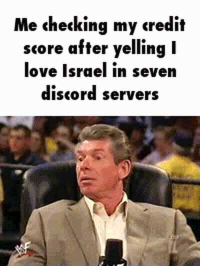 A Man In A Suit Is Sitting In A Chair With A Microphone In Front Of A Crowd . GIF