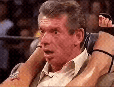 A Man In A Suit Is Sitting In A Chair With A Woman 'S Legs On His Shoulders . GIF