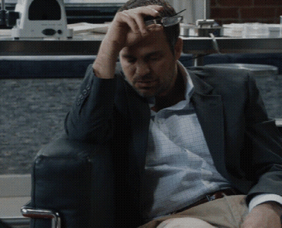 A Man In A Suit Is Sitting In A Chair With His Hand On His Forehead GIF