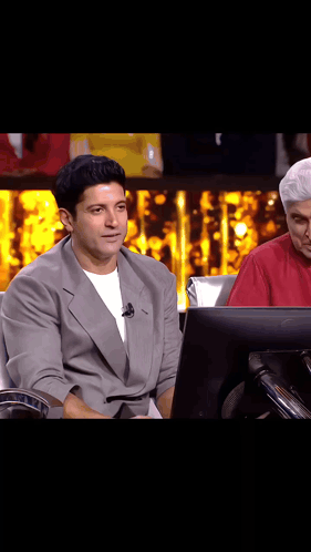 A Man In A Suit Is Sitting In Front Of A Computer Monitor On A Stage . GIF