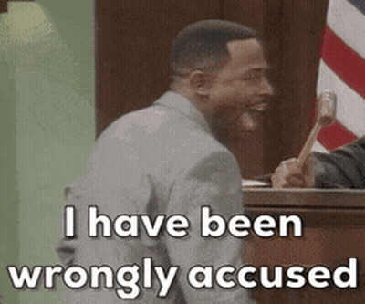 A Man In A Suit Is Sitting In Front Of A Judge Holding A Hammer . GIF