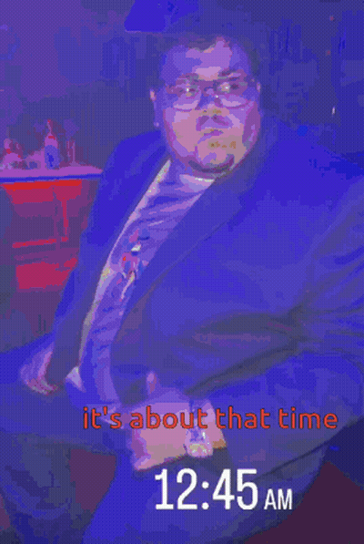 A Man In A Suit Is Sitting In Front Of A Sign That Says It 'S About That Time GIF