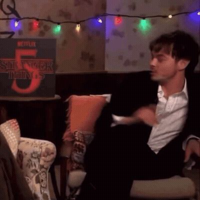 A Man In A Suit Is Sitting In Front Of A Stranger Things 5 Poster GIF