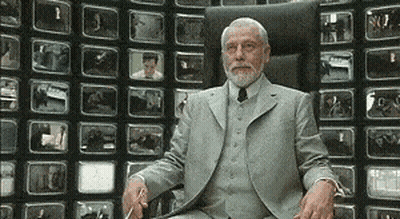 A Man In A Suit Is Sitting In Front Of A Wall Of Televisions . GIF