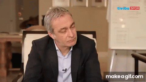 A Man In A Suit Is Sitting In Front Of A White Board That Says Tivibu Spor On It GIF