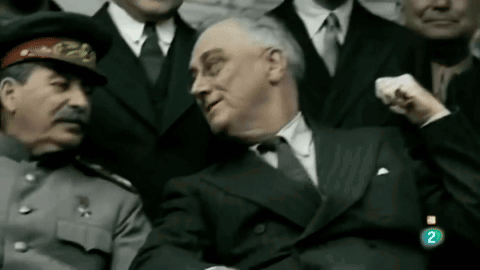A Man In A Suit Is Sitting Next To A Man In A Hat With The Number 2 On The Bottom Right GIF
