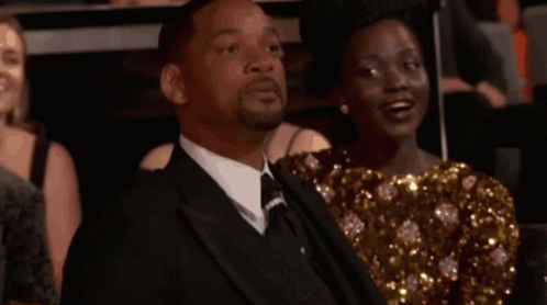 A Man In A Suit Is Sitting Next To A Woman In A Dress . GIF