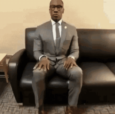 A Man In A Suit Is Sitting On A Couch . GIF