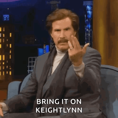 A Man In A Suit Is Sitting On A Couch And Giving The Middle Finger While Saying Bring It On Keightlynn . GIF