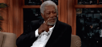 A Man In A Suit Is Sitting On A Couch And Pointing At His Face GIF