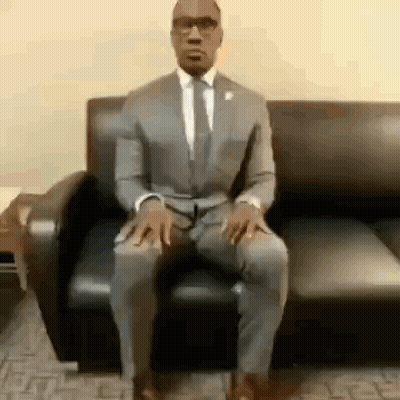 A Man In A Suit Is Sitting On A Couch . GIF