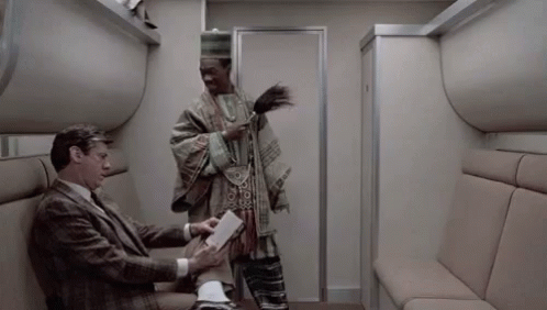 A Man In A Suit Is Sitting On A Couch Next To A Man In A Poncho . GIF