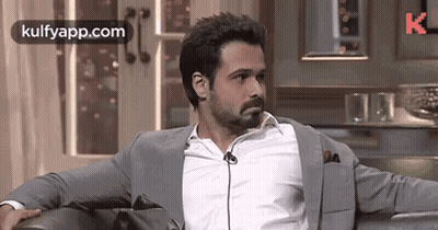 A Man In A Suit Is Sitting On A Couch With His Arms Crossed . GIF