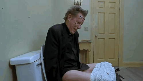 A Man In A Suit Is Sitting On A Toilet With His Pants Down And His Face Covered In Spots . GIF