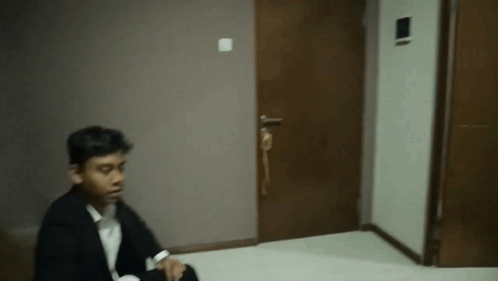A Man In A Suit Is Sitting On The Floor In Front Of A Door In A Dark Room . GIF