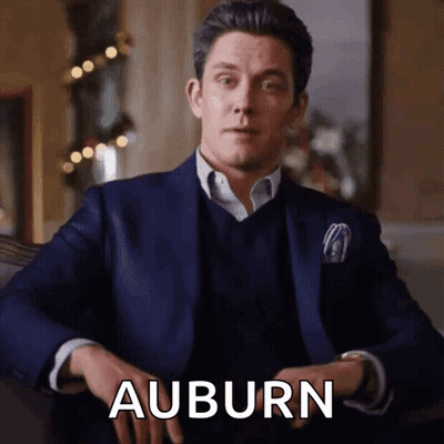 A Man In A Suit Is Sitting With His Hands Folded And The Word Auburn Is Visible GIF