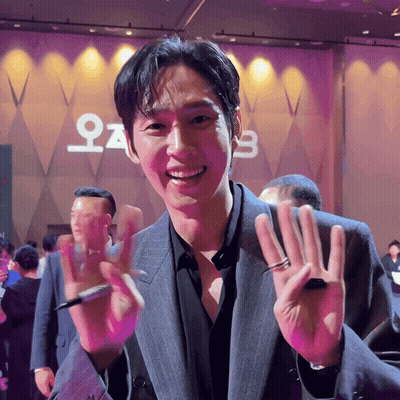 A Man In A Suit Is Smiling In Front Of A Sign That Says ' O ' On It GIF