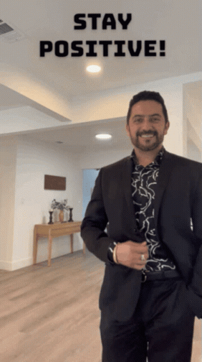 A Man In A Suit Is Smiling In Front Of A Sign That Says Stay Positive GIF