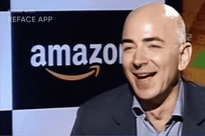A Man In A Suit Is Smiling In Front Of An Amazon Logo GIF