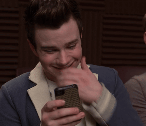 A Man In A Suit Is Smiling While Looking At His Cell Phone GIF