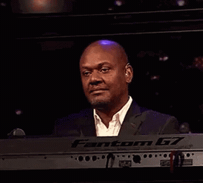 A Man In A Suit Is Smiling While Sitting At A Keyboard . GIF