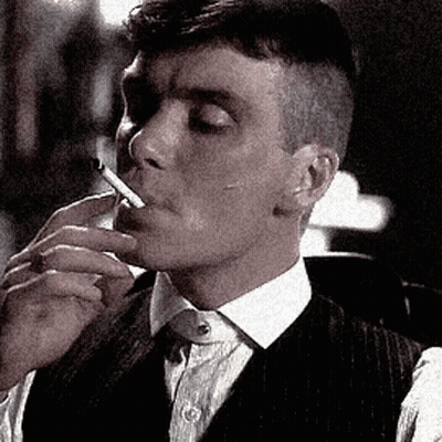 A Man In A Suit Is Smoking A Cigarette In A Black And White Photo . GIF