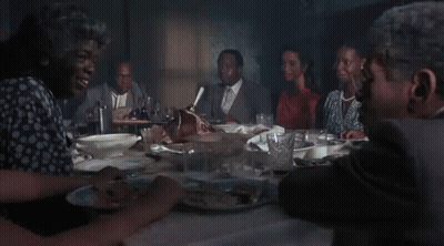 A Man In A Suit Is Smoking A Cigarette While Sitting At A Table With A Woman . GIF