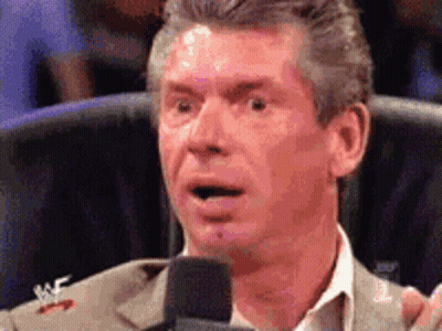 A Man In A Suit Is Speaking Into A Microphone With A Wrestler Logo On His Jacket GIF