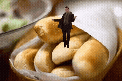 A Man In A Suit Is Standing In A Basket Of Bread GIF