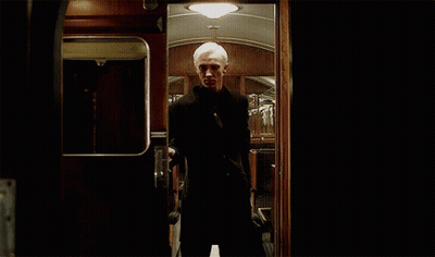 A Man In A Suit Is Standing In A Dark Room Behind A Door . GIF