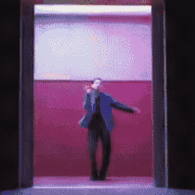 A Man In A Suit Is Standing In A Doorway With A Pink Wall Behind Him GIF