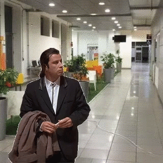 A Man In A Suit Is Standing In A Hallway Holding A Jacket GIF