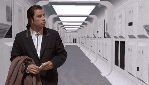 A Man In A Suit Is Standing In A Hallway With Lockers GIF