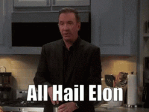 A Man In A Suit Is Standing In A Kitchen With The Words All Hail Elon On The Counter GIF