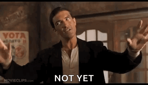 A Man In A Suit Is Standing In A Room With His Arms Outstretched And A Sign That Says Not Yet . GIF