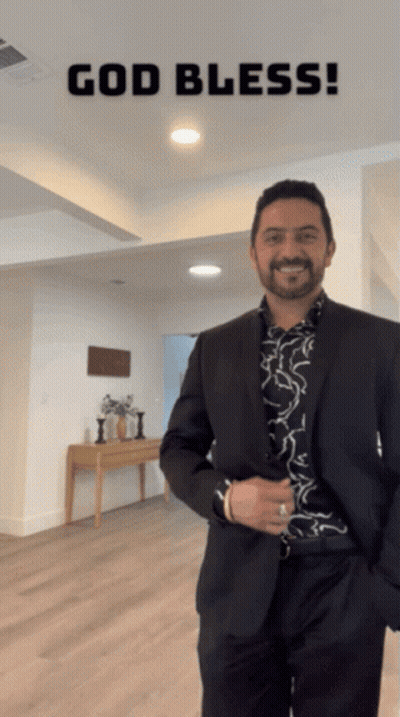 A Man In A Suit Is Standing In A Room With The Words God Bless Written Above Him GIF