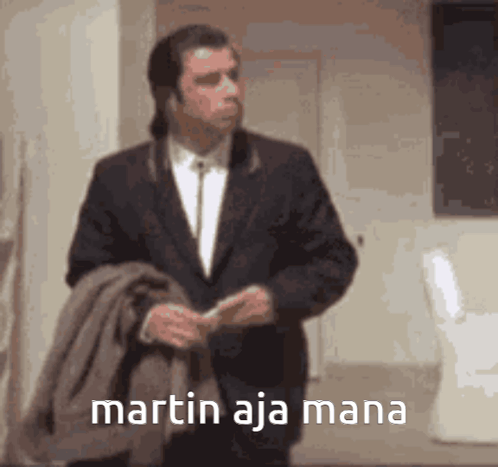 A Man In A Suit Is Standing In A Room With The Words Martin Aja Mana Written On The Screen GIF