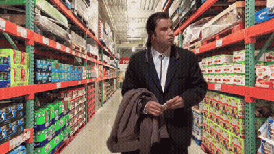 A Man In A Suit Is Standing In A Store Aisle With A Sign That Says ' Pri ' On It GIF