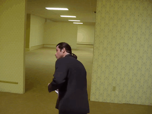 A Man In A Suit Is Standing In An Empty Room And Pointing GIF