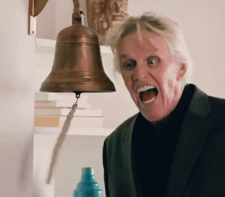 A Man In A Suit Is Standing In Front Of A Bell With His Mouth Open GIF
