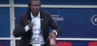 A Man In A Suit Is Standing In Front Of A Blue Wall And Holding A Bottle Of Water . GIF