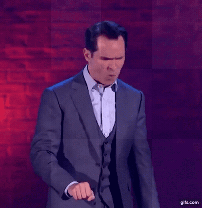 A Man In A Suit Is Standing In Front Of A Brick Wall And Making A Funny Face . GIF