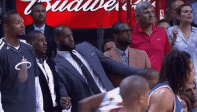 A Man In A Suit Is Standing In Front Of A Budweiser Sign . GIF
