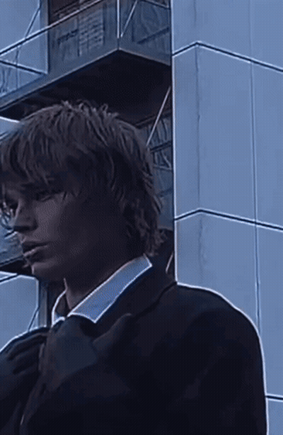 A Man In A Suit Is Standing In Front Of A Building . GIF